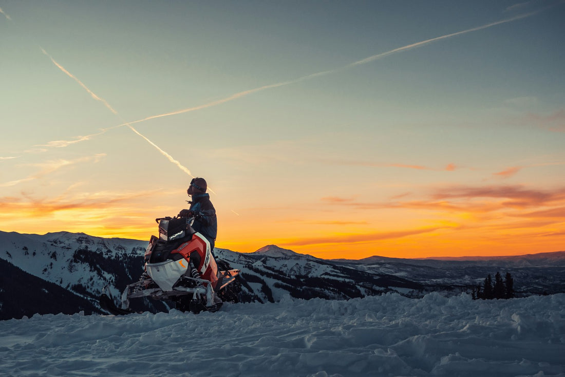 Snowmobile riders pausing at sunset on a winter ridge